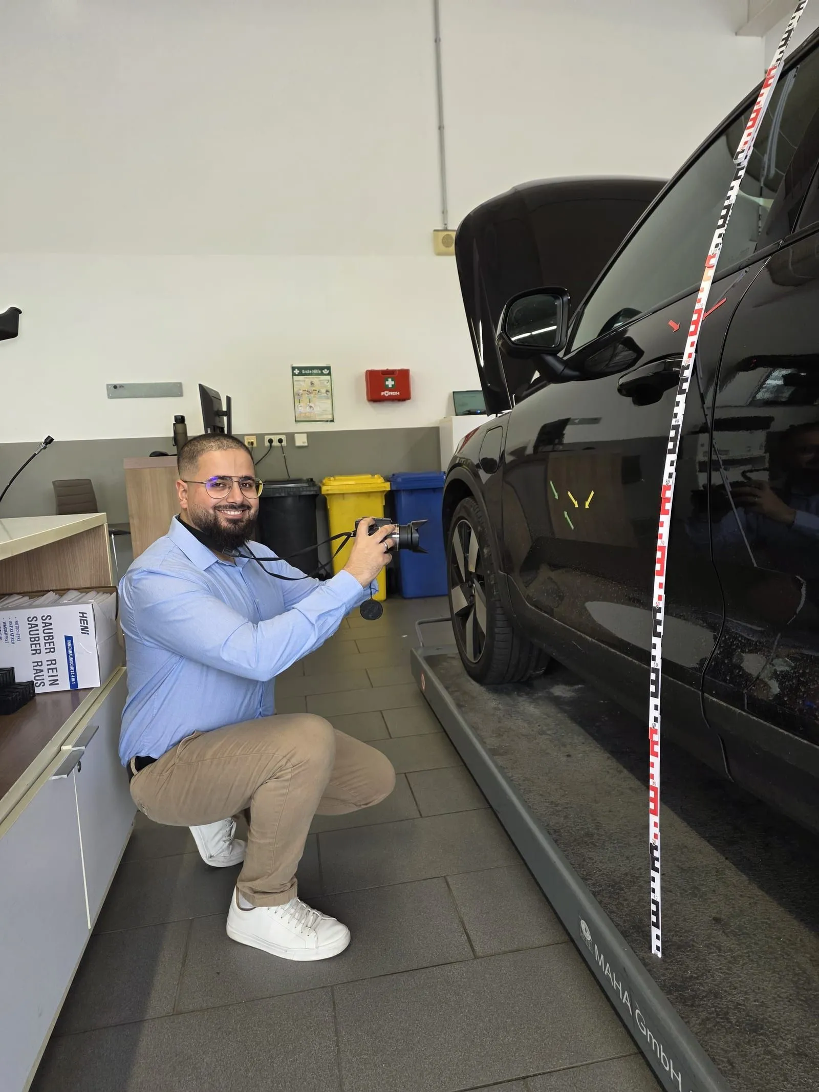 Muhammed Erdogdu nimmt einen Fahrzeugschaden mit der Kamera auf, daneben eine Messlatte am Fahrzeug.