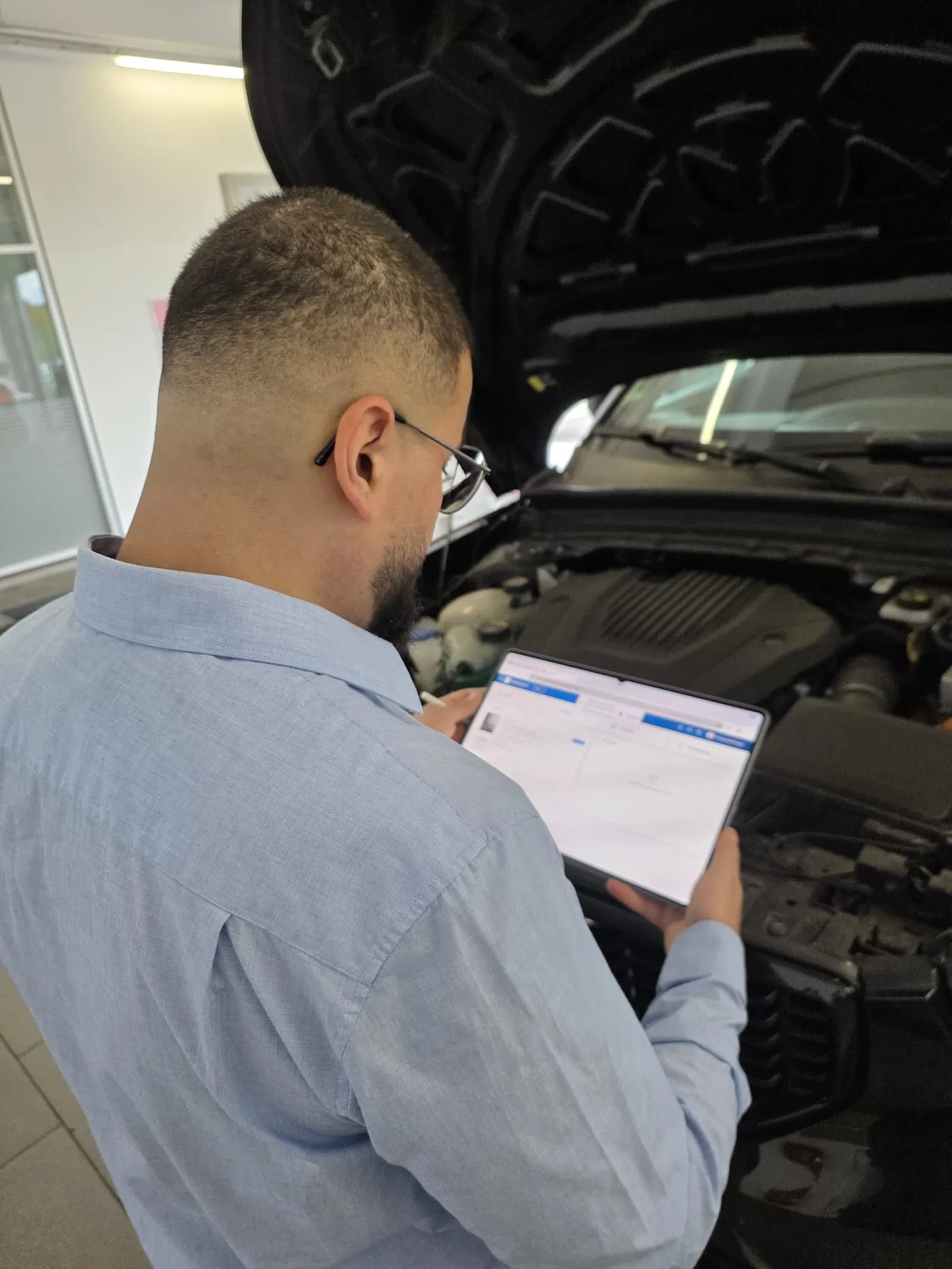 Muhammed Erdogdu trägt die Schadenaufnahme am Tablet ein, davor die geöffnete Motorhaube.